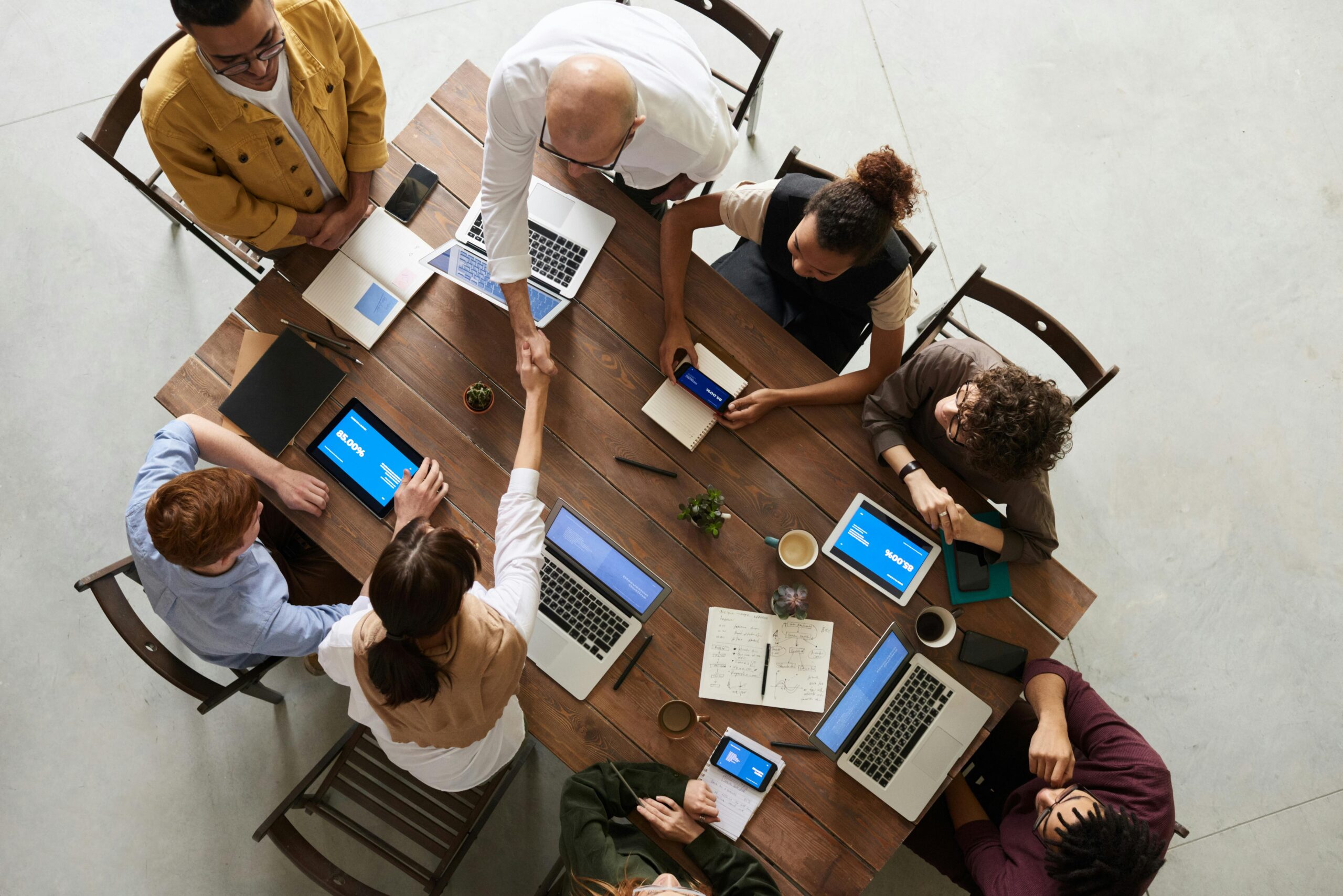5 leviers pour réussir le re-onboarding après un arrêt long. Top view of a diverse team collaborating in an office setting with laptops and tablets, promoting cooperation.