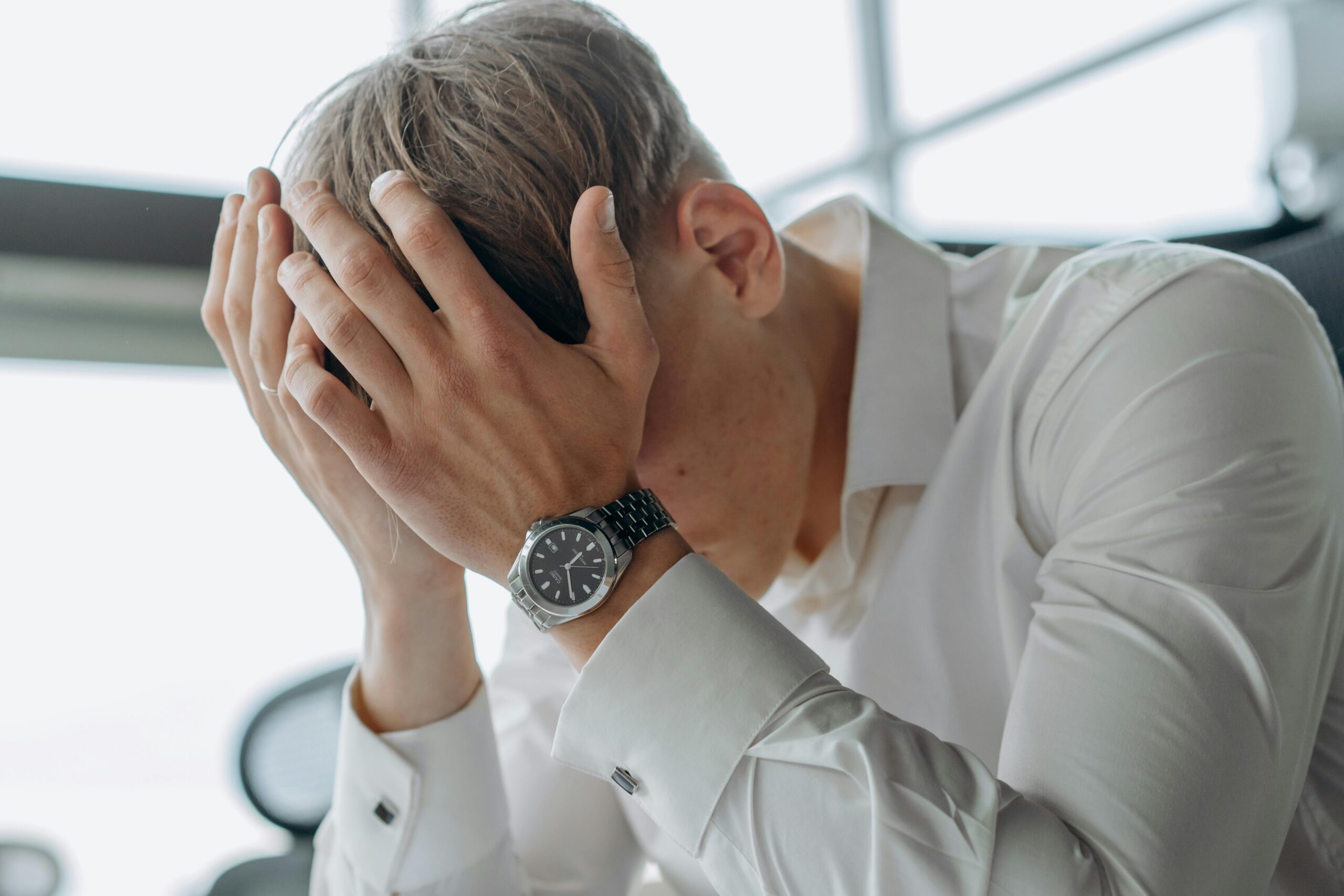 Gérer le stress en entreprise : pourquoi la sophrologie est un allié de poids. A business professional showing stress and fatigue with head in hands.